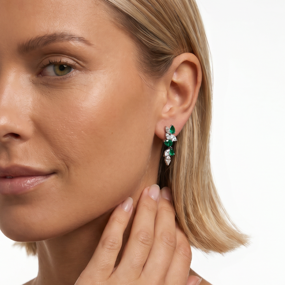 Modelo llevando pendientes largos de plata de ley 925 con baño en rodio y circonitas blancas y verde esmeralda de NILU.